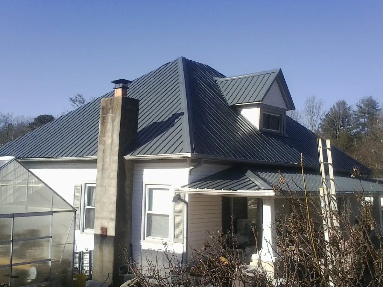 Dark blue standing seam metal roof on a white farmhouse with dormer — Slate & Tile Roof Repair by Roofing Brothers in Wainscott