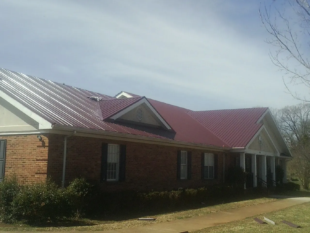 Red metal roof with gabled entries on a long brick building, from a Hail Damage Roof Repair job in Wainscott