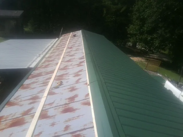 Old rusted panels beside newly installed green metal roofing — Wind Damage Roof Repair by Roofing Brothers in Wainscott
