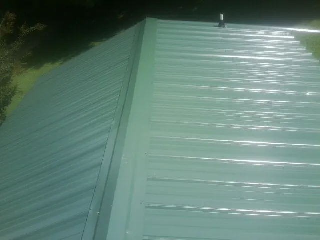 New green metal panels meeting at the ridge of a roof — Flat Roof Repair work by our crew in Wainscott