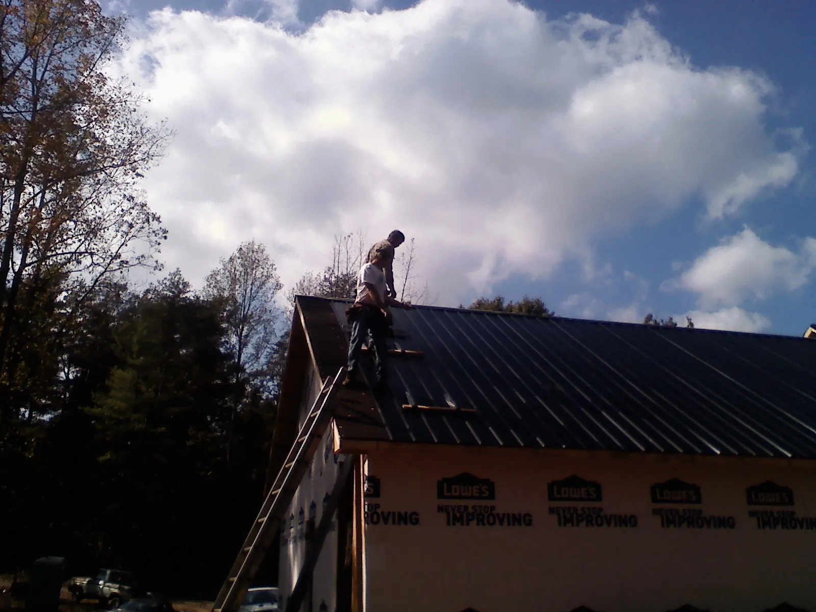 Roofer fastening dark metal panels high against a cloudy sky, from a Roof Inspection job in Wainscott