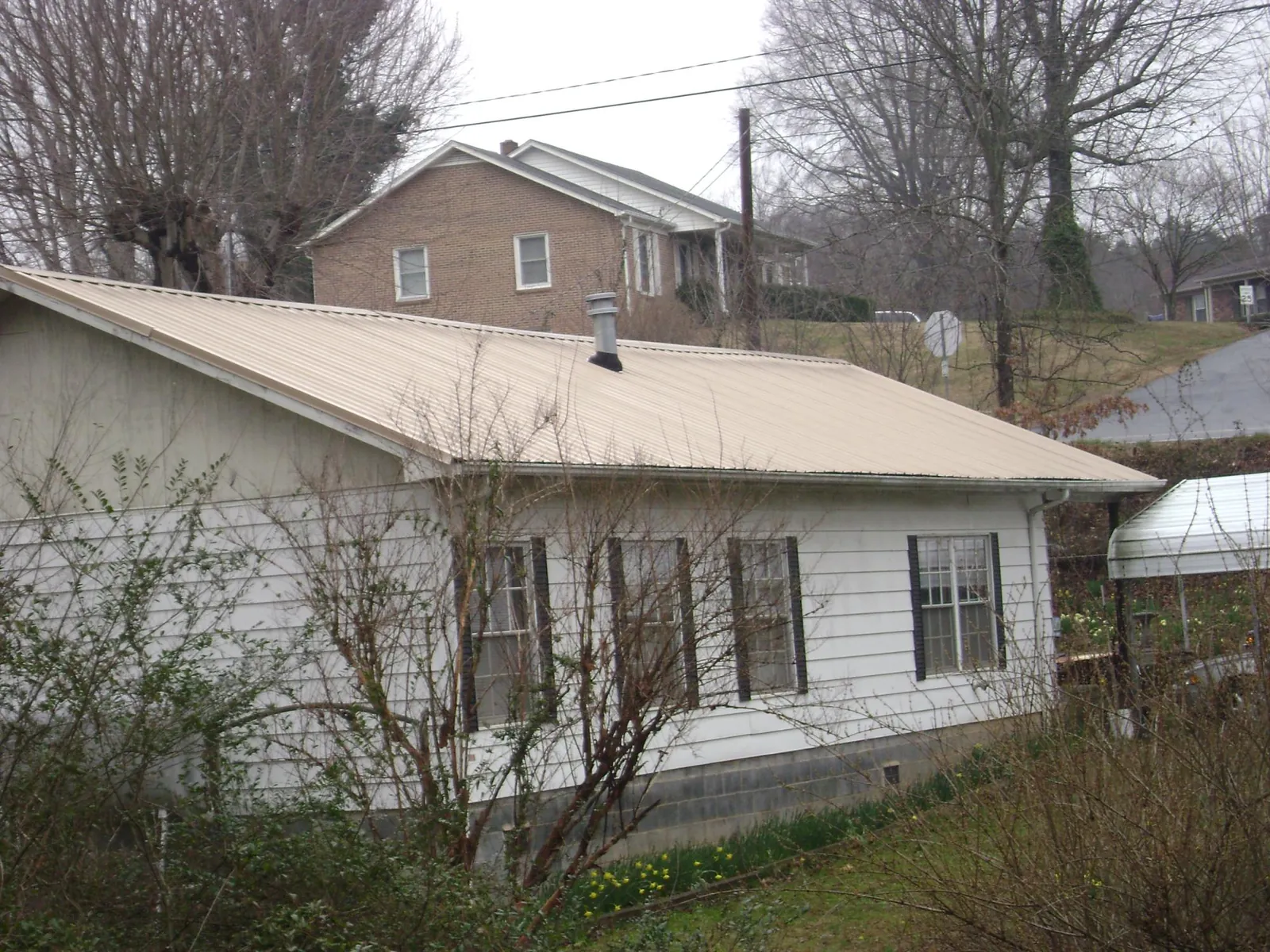 Tan metal roof on a white sided house set into a hillside — Commercial Roofing by Roofing Brothers in Wainscott